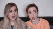 two women are sitting on a couch with their mouths open and making funny faces .