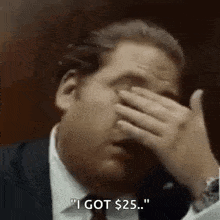 a man in a suit and tie is covering his face with his hand and says `` i got $ 25 . ''