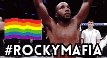 a shirtless boxer stands in front of a rainbow flag with #rockymafia written below him