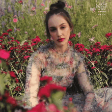 a woman in a floral dress sits in a field of flowers with a lakme fashion week next advertisement behind her