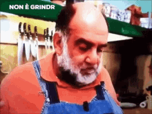 a bald man with a beard is wearing overalls in a kitchen with the words non e grindr above him .