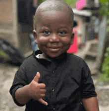 a young boy in a black shirt is giving a thumbs up .