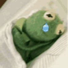 a kermit the frog is laying in bed with a tear coming out of its eye .