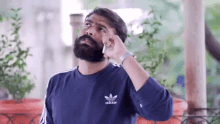 a man with a beard is wearing a blue adidas sweatshirt and talking on a cell phone .