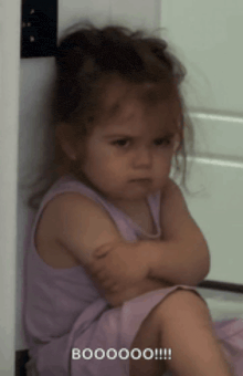 a little girl in a purple dress is sitting on the floor with her arms crossed and the words boooooo !!! written below her