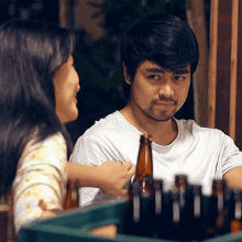 a man with a beard holds a bottle of beer while talking to a woman