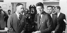 a black and white photo of a man in a suit and tie standing next to a man in a suit and tie