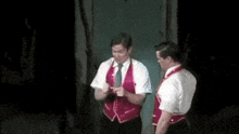 two men in red vests and ties are standing next to each other on a stage in a dark room .