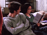 a man and a woman sit on a couch reading books