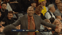 a man in a suit and tie stands in front of a crowd watching a basketball game between pacers and nets