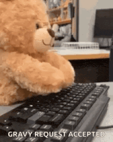 a teddy bear is sitting at a desk typing on a computer keyboard .