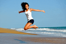 a woman jumps in the air on a beach wearing a white tank top that says " freedom "