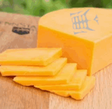 a piece of cheese is sitting on a wooden cutting board with slices of cheese on it .