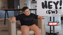 a young boy sits in a chair in front of a sign that says hey