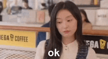 a woman is sitting at a table in front of a sign that says coffee .
