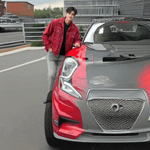 a man in a red jacket leans on the hood of a car