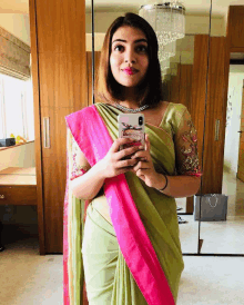 a woman in a green and pink saree is taking a selfie with her phone