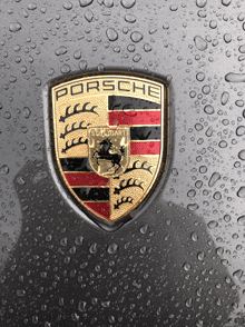 a porsche emblem is on a gray surface with water drops