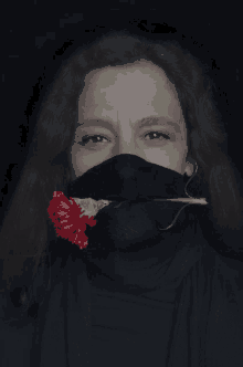 a woman wearing a black face mask holds a red carnation in her mouth