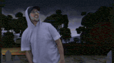 a man wearing a hoodie stands in front of a cemetery at night