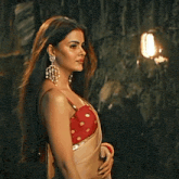 a woman wearing a red top and earrings stands in front of a dark wall