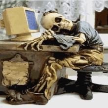 a statue of a skeleton sitting at a desk with a computer monitor