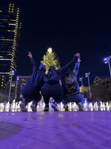 three people are posing for a picture in front of a christmas tree and fountain