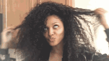 a woman with curly hair is holding her hair in her hand and making a funny face .