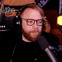 a man wearing headphones and glasses talks into a microphone in front of a chair that says writer on it