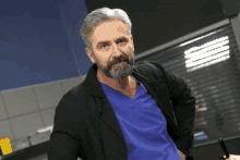 a man with gray hair and a beard is wearing a blue scrub top and black jacket