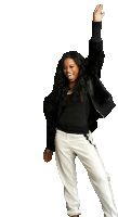 a woman wearing a black jacket and white pants is raising her arm in the air