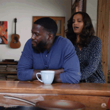 a man and a woman are sitting at a table with a cup of coffee and a nbc logo in the background