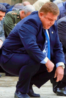 a man in a suit and tie is squatting down and adjusting his shoes