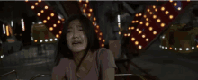 a woman in a pink shirt is crying in front of a carousel