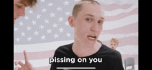 a man in a black shirt says pissing on you in front of an american flag