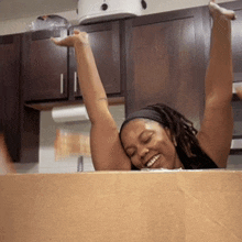 a woman is sitting in a cardboard box with her arms up