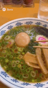 a close up of a bowl of ramen with a picture of sora on the bottom