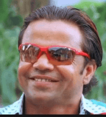 a man wearing red sunglasses is smiling and making a funny face .