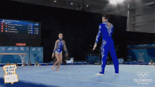 a man and a woman are standing on a balance beam in front of a screen that says olympic channel