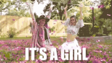 two women are standing in a field of pink flowers with the words `` it 's a girl '' written above them .