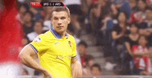 a soccer player in a yellow and blue jersey stands in front of a crowd during a match between urd and ars