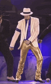 a man in a white hat and gold pants is dancing on stage