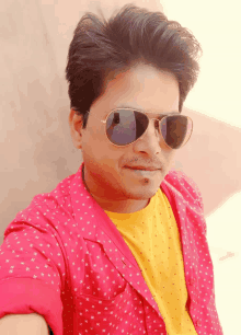 a man wearing sunglasses and a pink shirt is looking at the camera