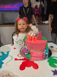 a little girl is sitting at a table with a pink cake with the number 4 on top