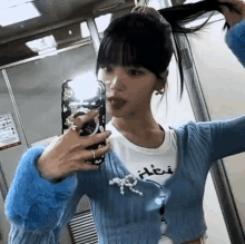 a woman is taking a selfie in front of a mirror while wearing a blue cardigan .