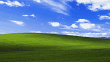 a grassy hill with a blue sky and white clouds behind it