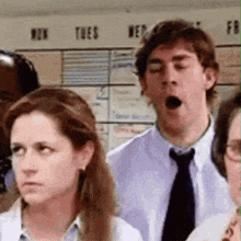 a man in a tie is yawning while standing in a crowd of people .
