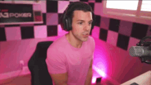 a man wearing headphones and a pink shirt sits in front of a microphone