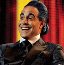 a man in a suit and tie is smiling in front of a red curtain ..