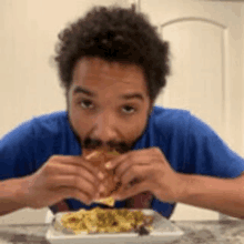 a man is sitting at a table eating a sandwich from a plate .